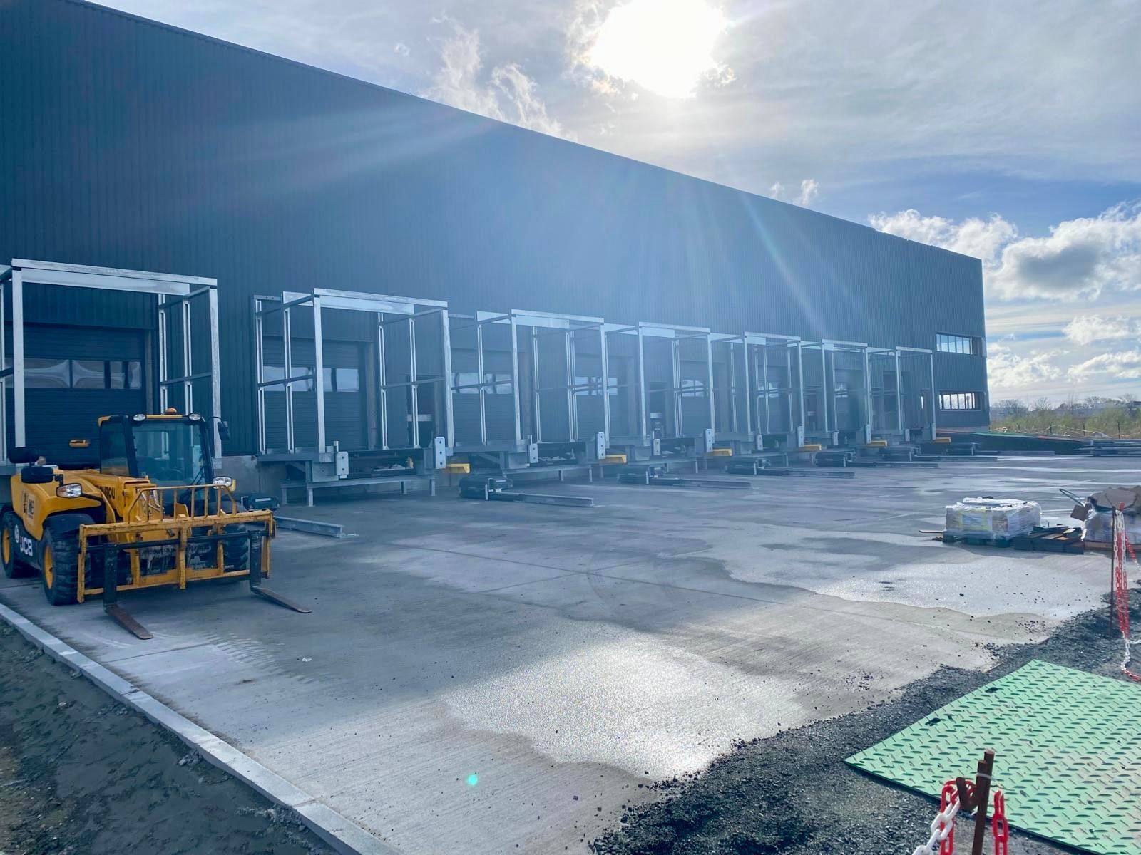 Des engins de chantier stationnés devant un grand entrepôt industriel par une journée ensoleillée