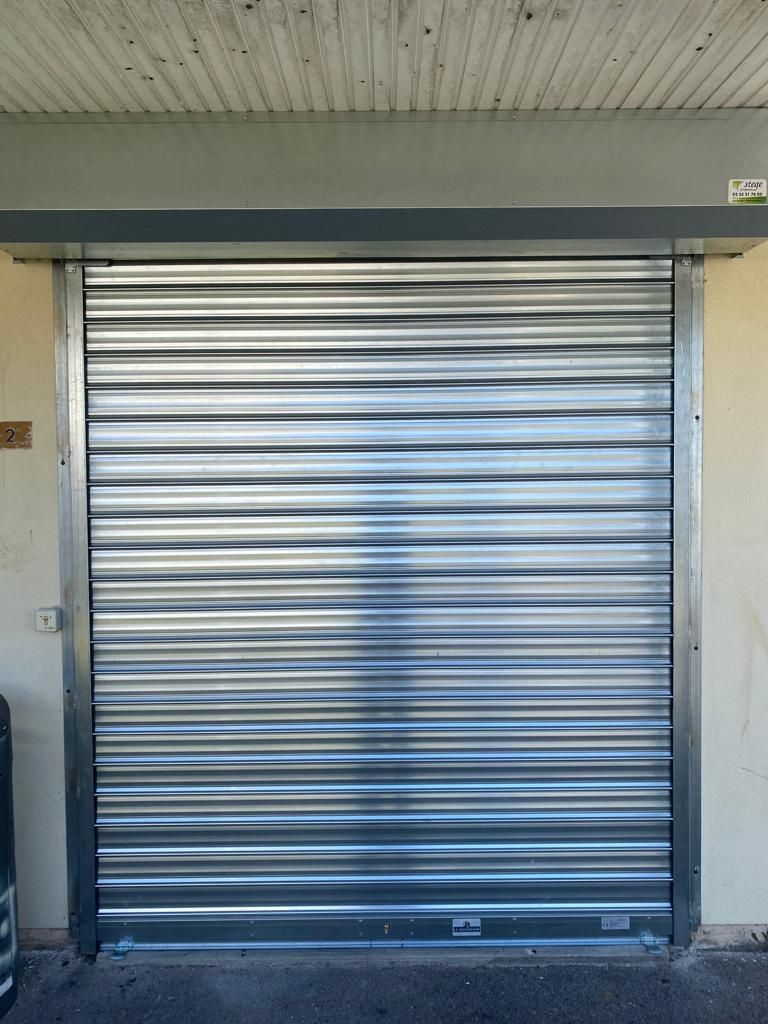 Porte sectionnelle métallique argentée fermée sous un auvent en béton.