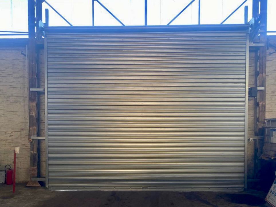 Porte de garage sectionnelle en métal gris, fermée, entre des murs en pierre sous un cadre bleu