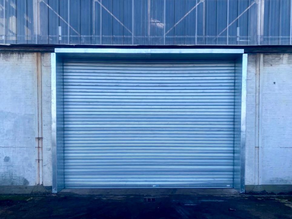 Porte de garage métallique argentée fermée, encastrée dans un mur en béton avec des finitions bleu-gris.