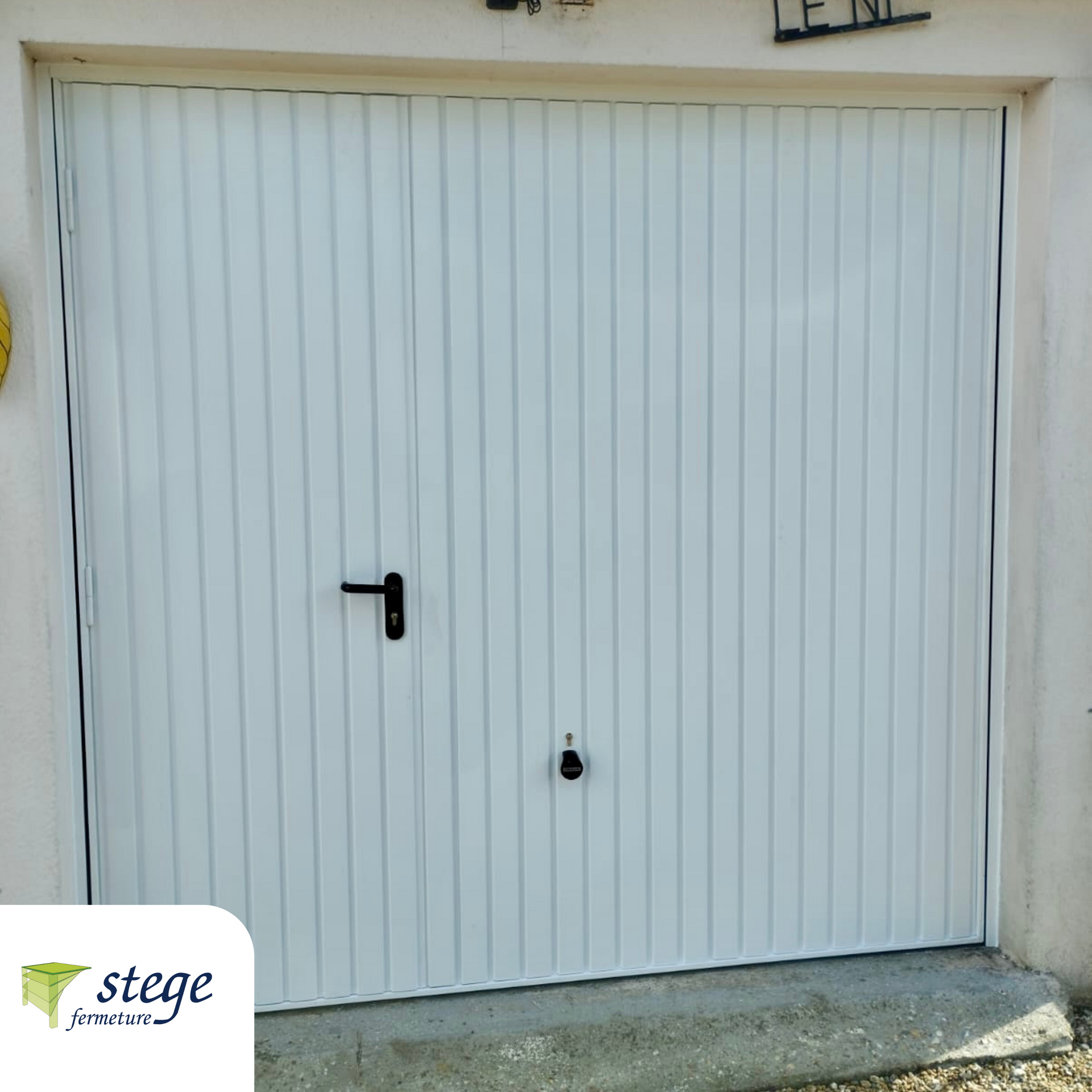 Porte de garage à panneaux blancs avec poignée et serrure noires, encastrée dans un mur en béton.