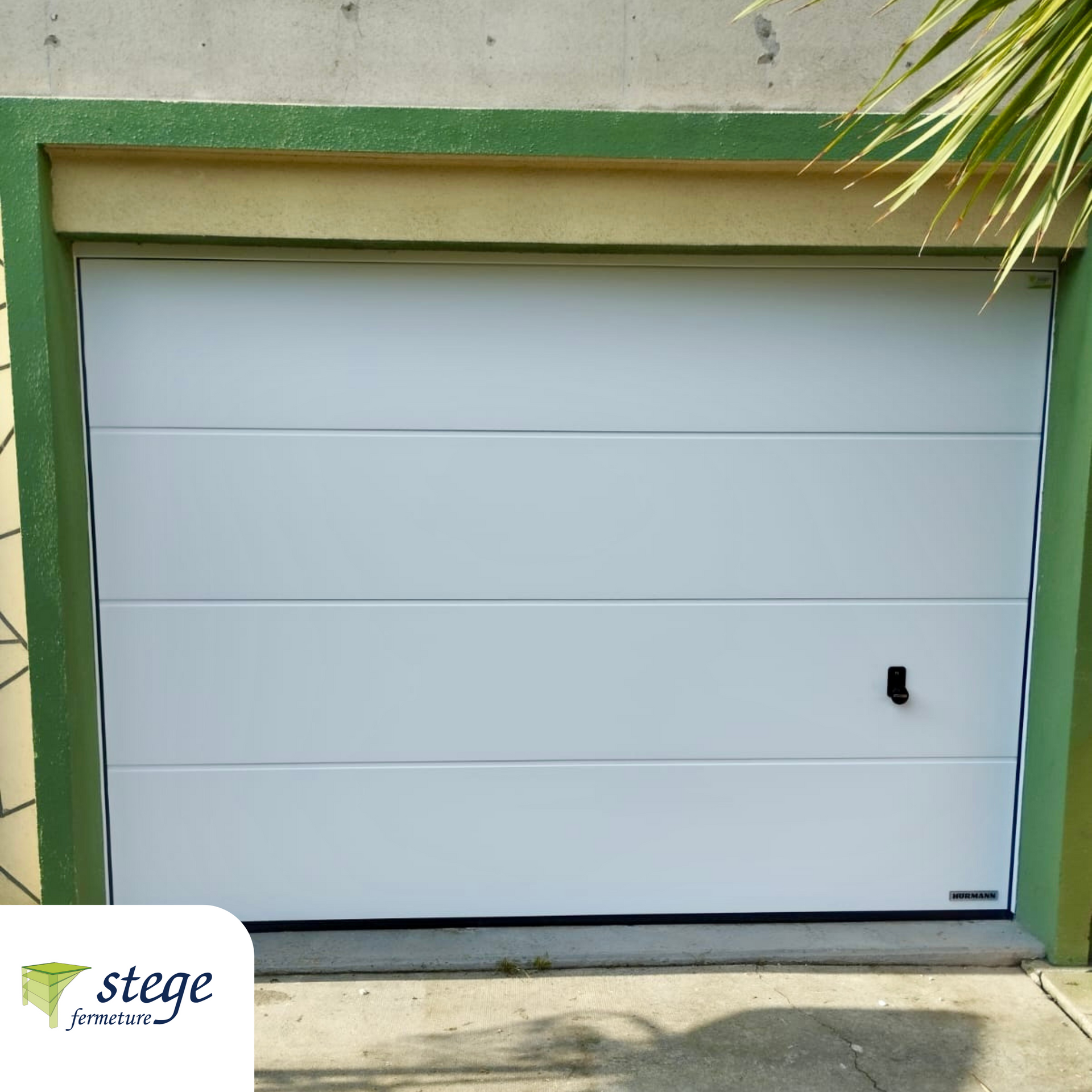 Porte de garage blanche avec garniture verte sur une maison en stuc, vue depuis l'allée.