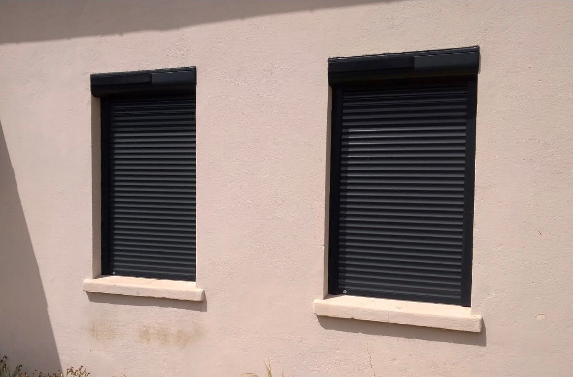 Deux volets noirs fermés sur un mur extérieur beige