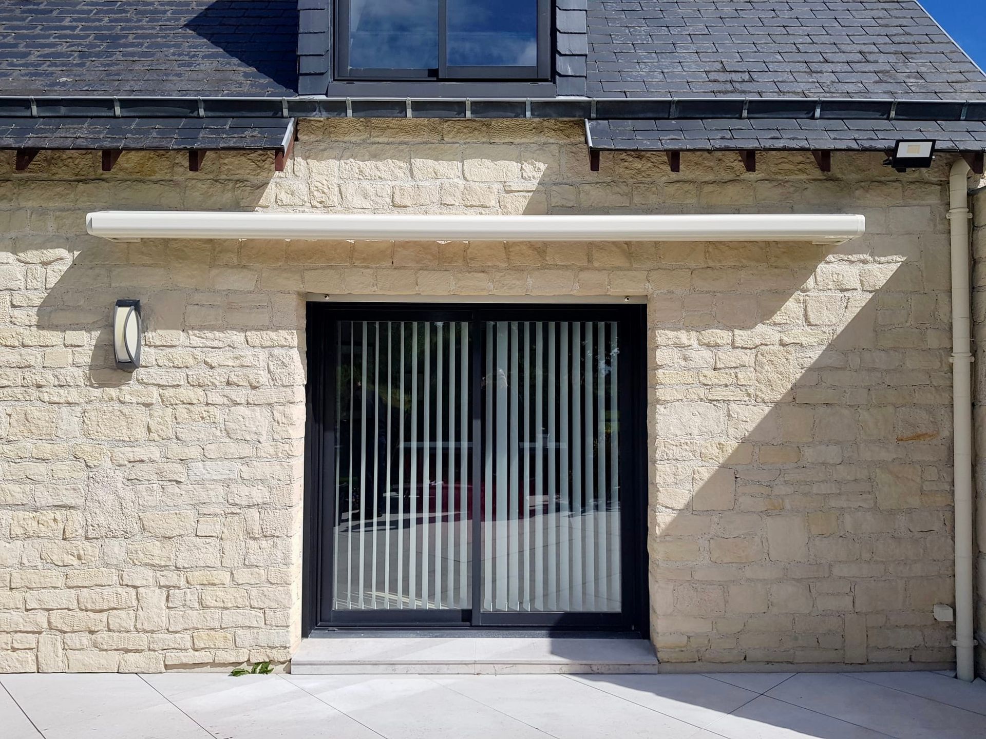 Maison en pierre avec porte-fenêtre coulissante et auvent blanc au soleil