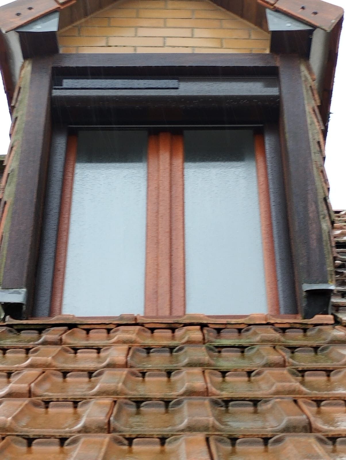 Vieille fenêtre de grenier avec verre dépoli et encadrement rouge au-dessus d'un toit de tuiles