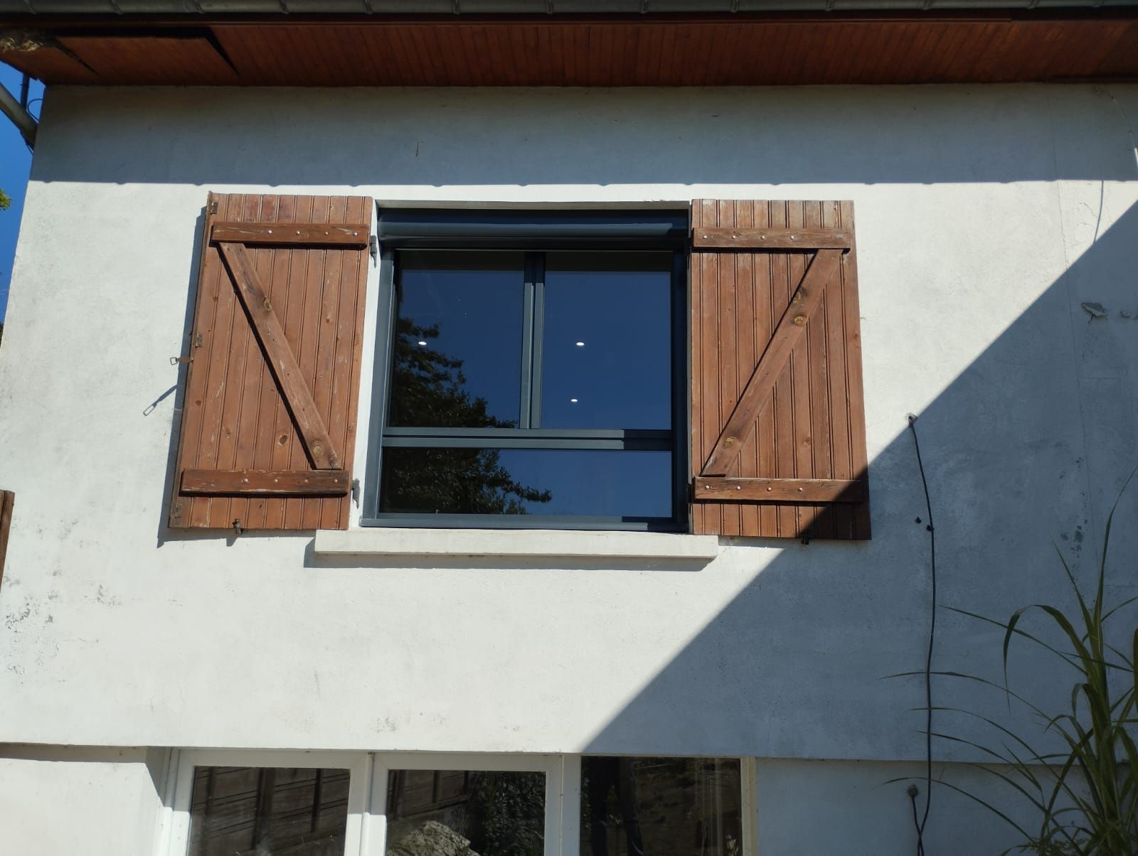 Façade de maison en stuc blanc avec une fenêtre centrale et des volets en bois ouverts au soleil