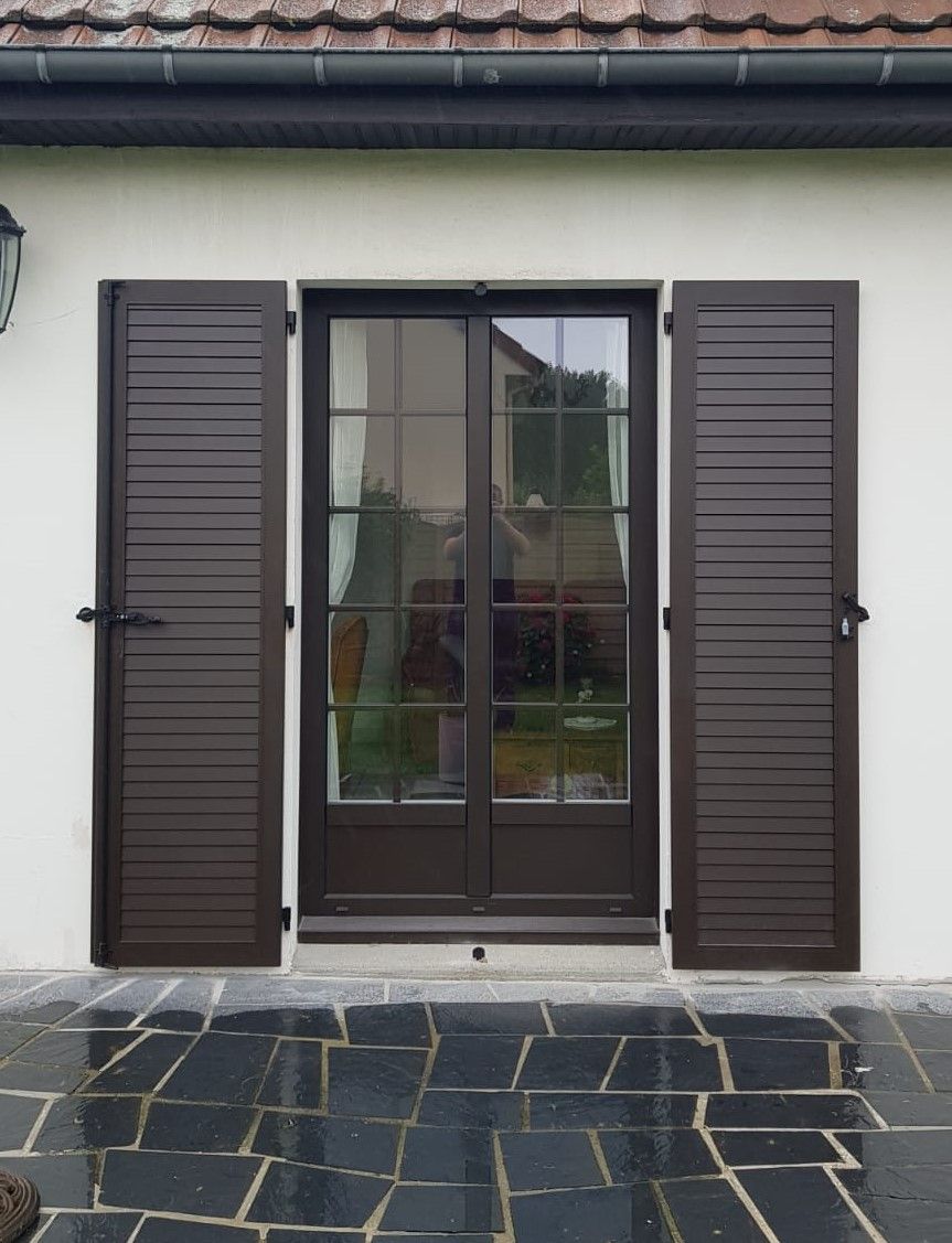 Porte d'entrée avec volets brun foncé et terrasse pavée devant