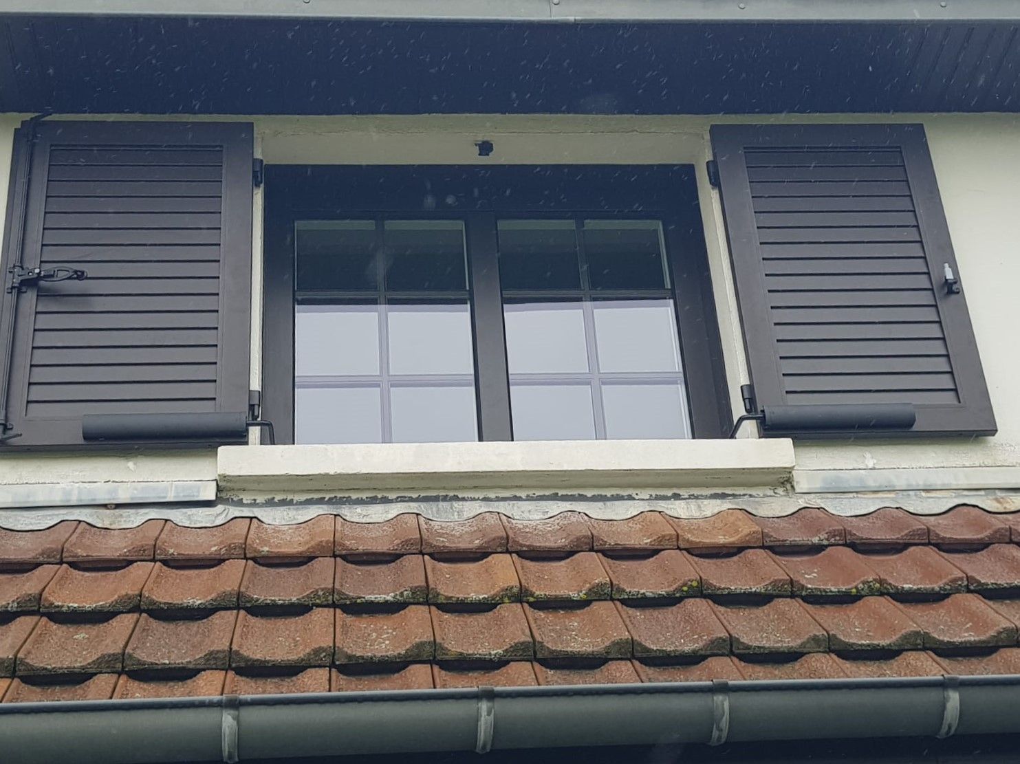 Fenêtre à volets gris au-dessus d'un toit de tuiles rouges sur l'extérieur d'une maison