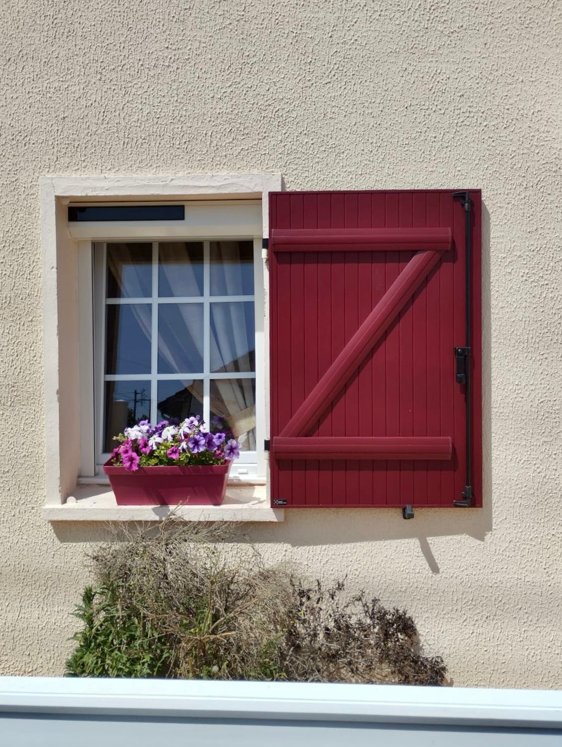 Volet rouge à côté d'une fenêtre avec une jardinière sur la façade d'une maison beige