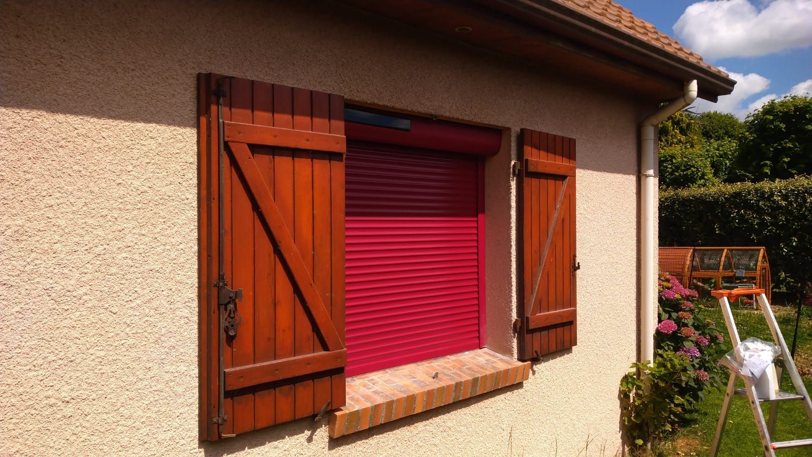 Façade de maison avec volets rouges et store vénitien rouge vif sur un mur en stuc.