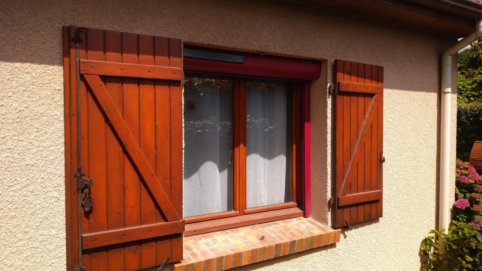 Gros plan sur une fenêtre de maison avec des volets en bois rouge et un appui de fenêtre en briques sur un mur en stuc beige