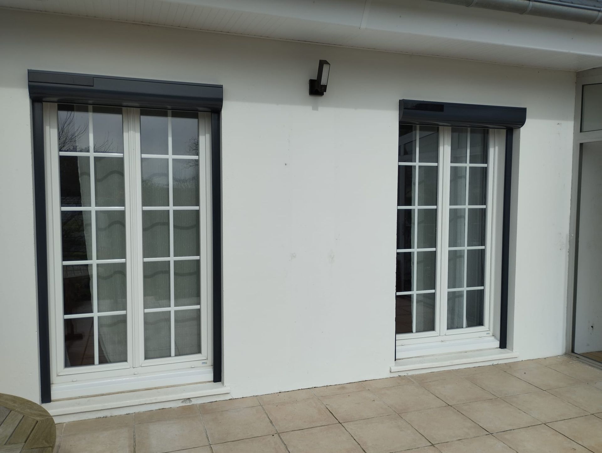 Mur extérieur blanc avec deux fenêtres à barreaux et une terrasse carrelée.