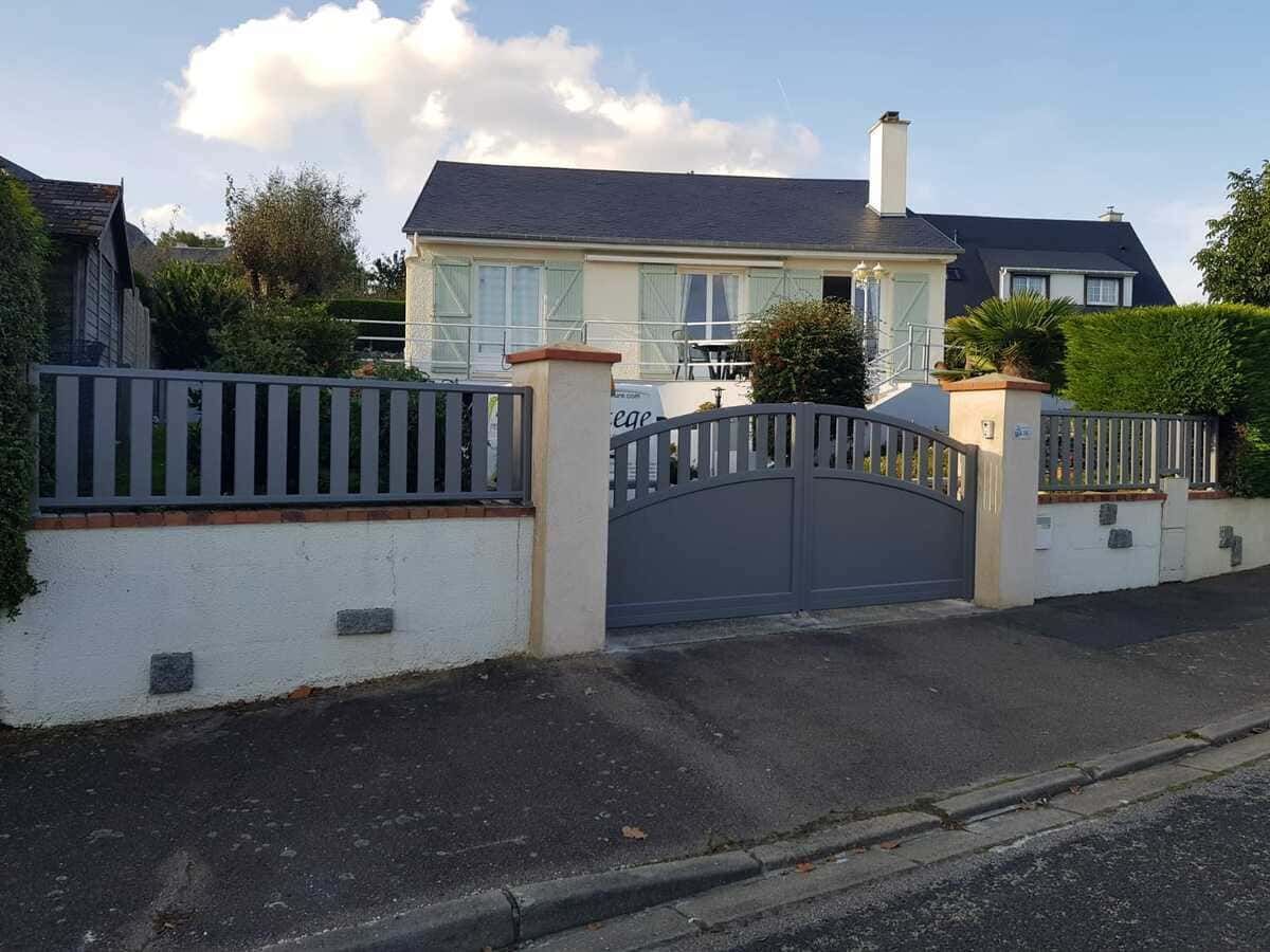Maison de banlieue avec portail gris et mur blanc le long d'une rue en pente