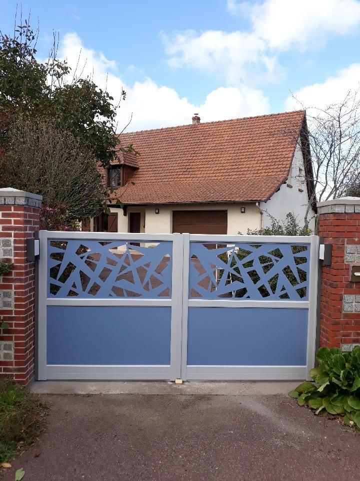Un portail bleu orné de panneaux décoratifs se dresse devant une petite maison au toit de tuiles rouges.