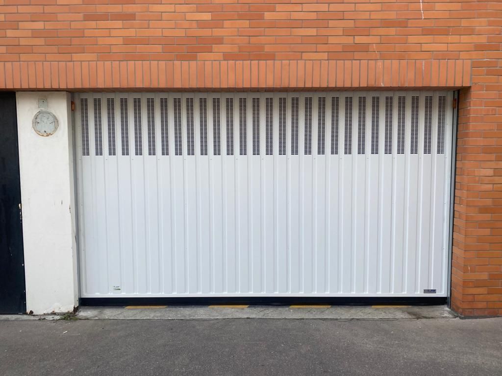 Porte de garage blanche à lames verticales encastrée dans une façade d'immeuble en briques