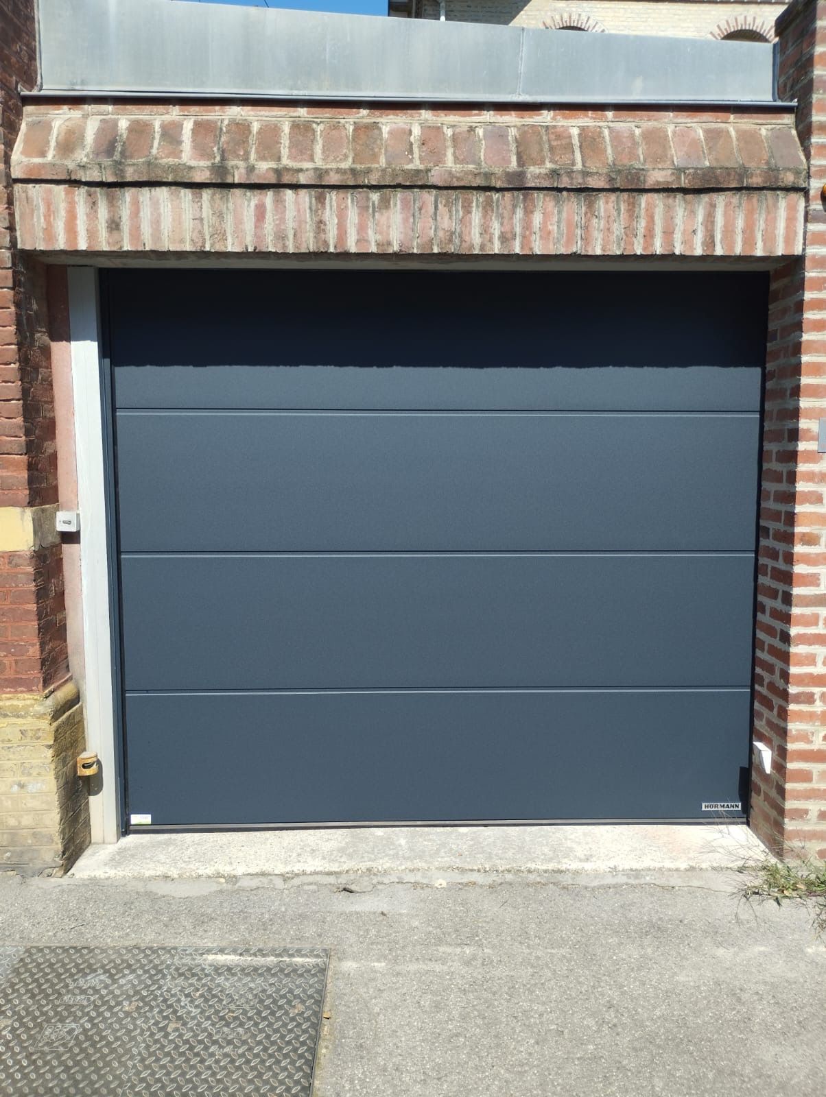 Porte de garage bleue sur la façade d'un bâtiment en briques avec une allée devant
