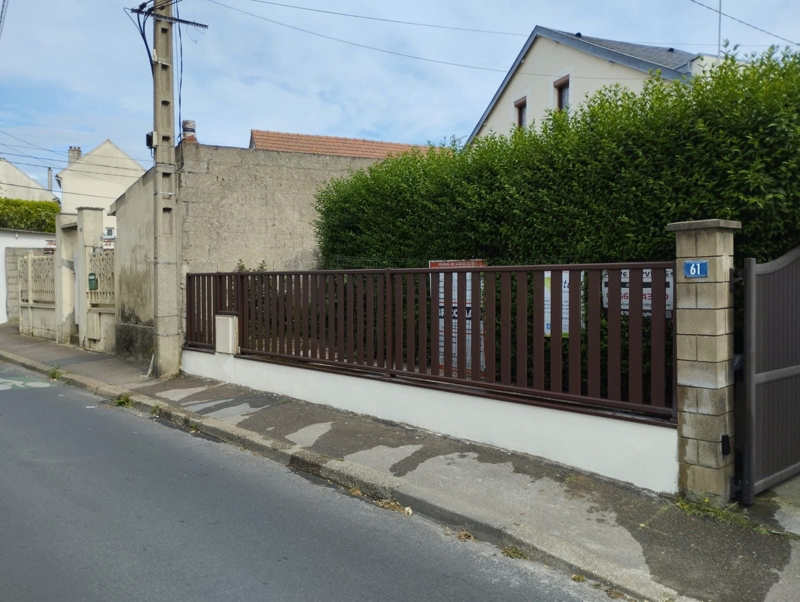Maison d'habitation avec portail marron et haie, située dans une rue calme.
