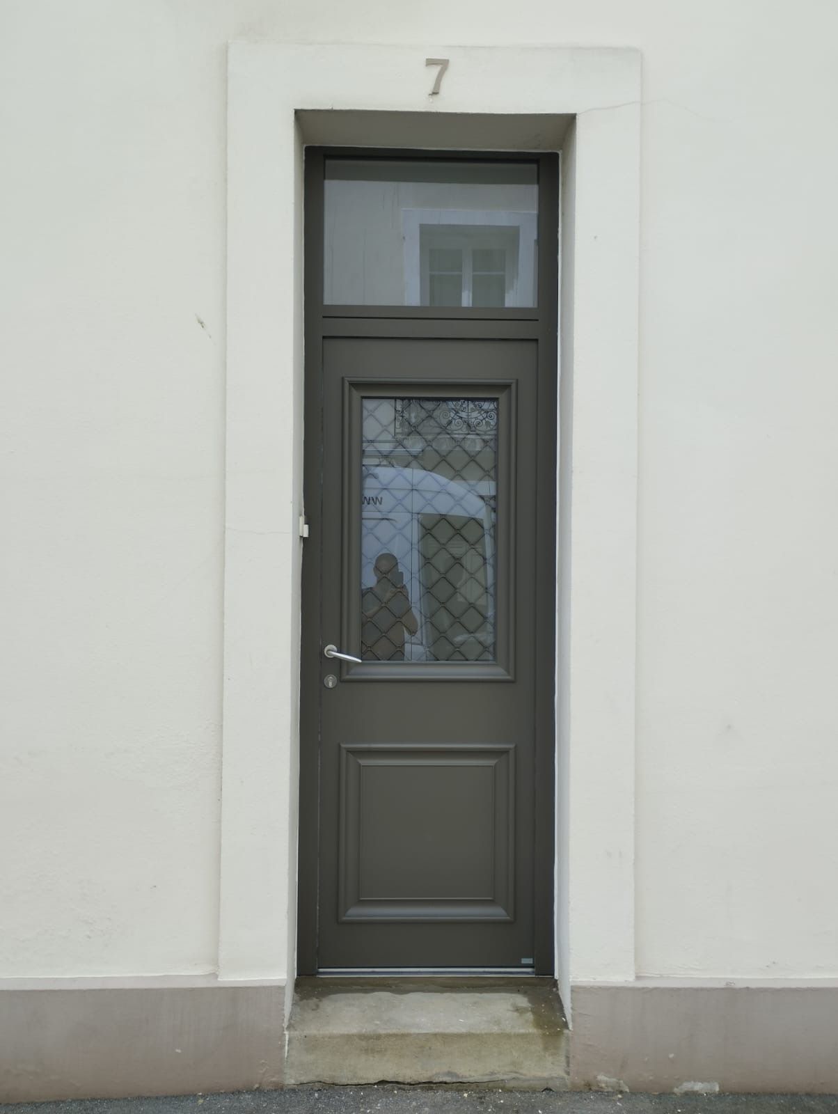 Porte grise avec une petite fenêtre et le chiffre 7 au-dessus, sur un mur blanc.
