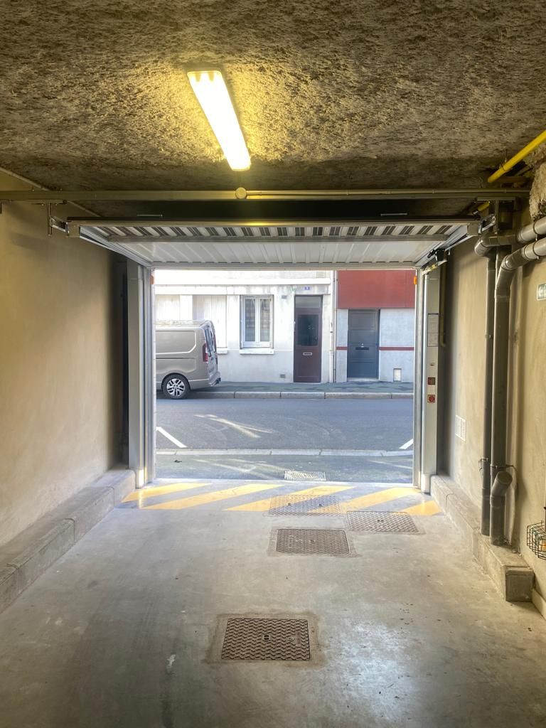Vue depuis l'entrée d'un garage sur une rue où des camionnettes sont garées et un bâtiment se trouve de l'autre côté de la rue.