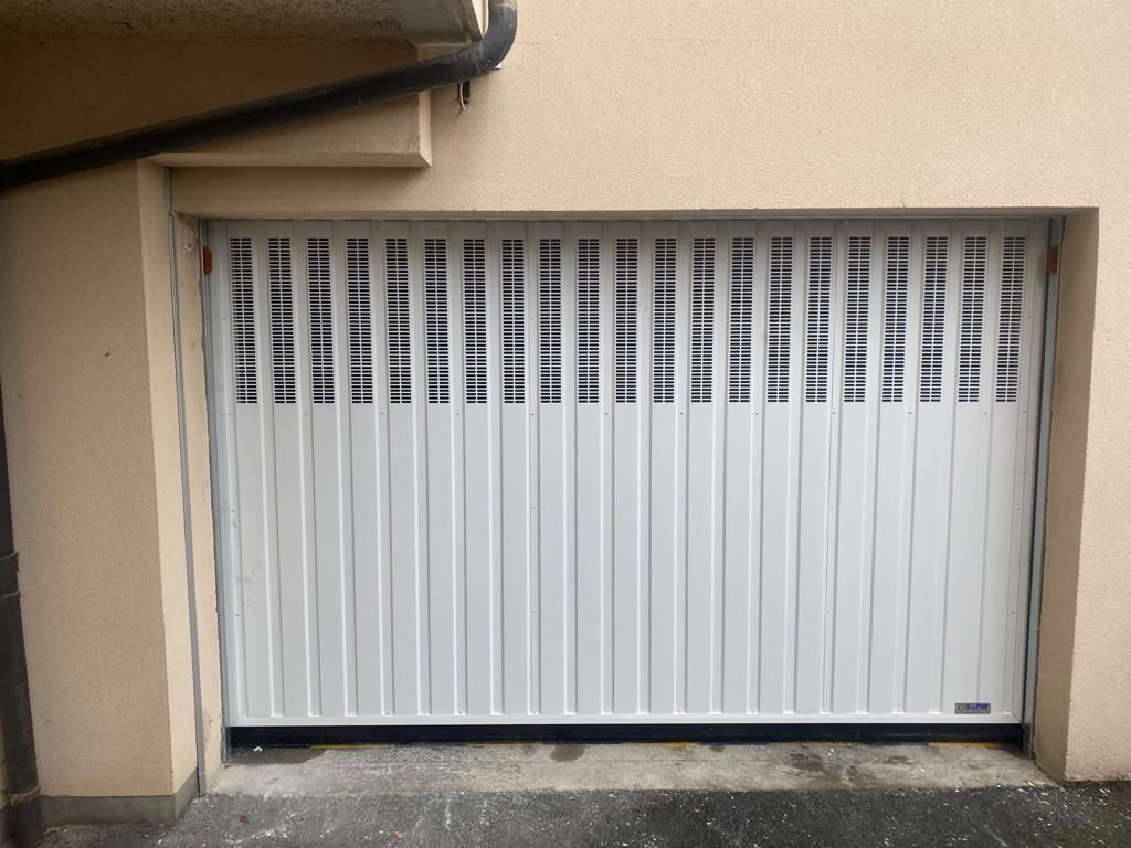 Porte de garage blanche à lamelles verticales sur un extérieur de bâtiment beige