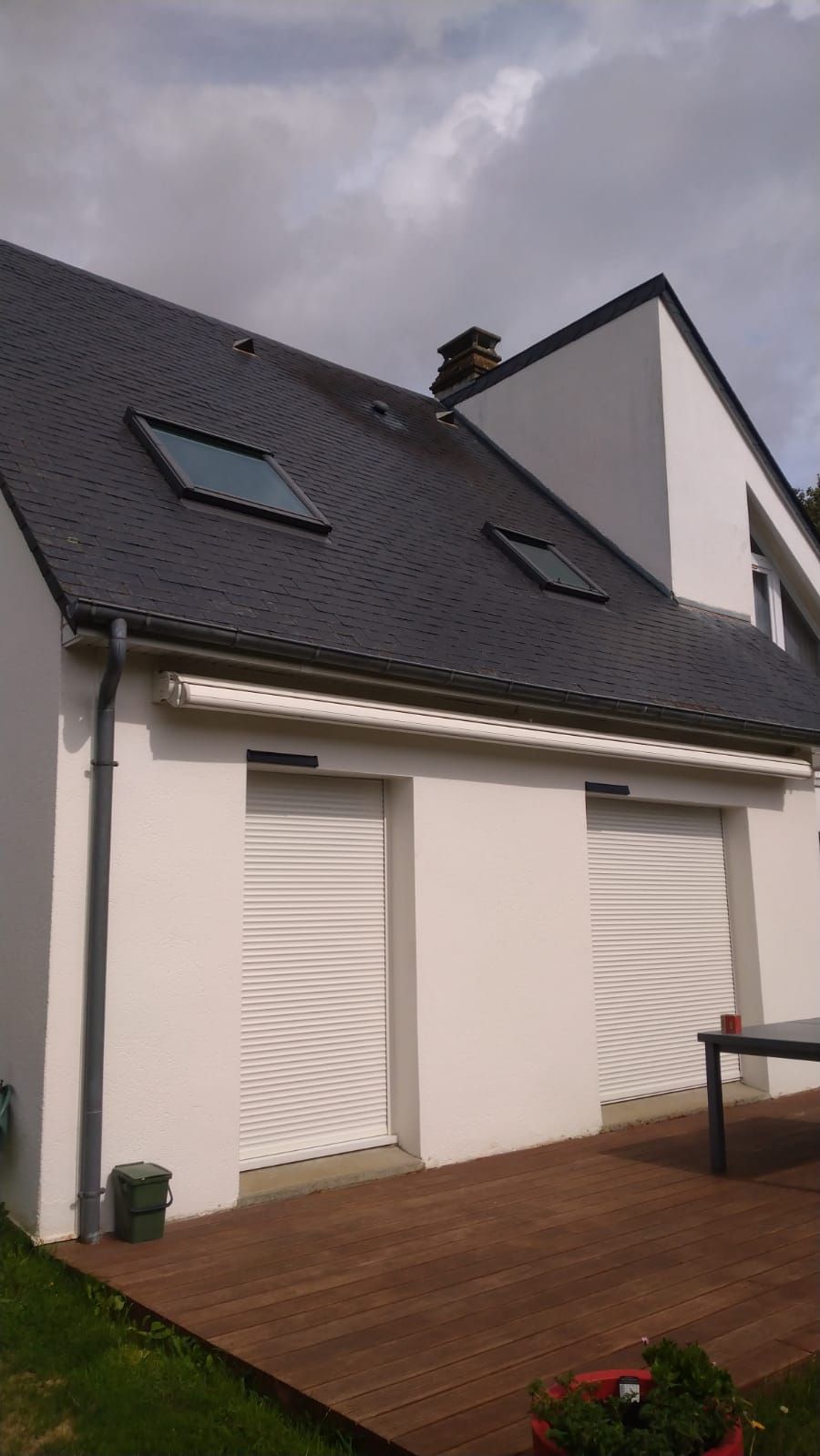 Maison blanche moderne avec toit gris foncé, fenêtres de toit et terrasse en bois à l'avant