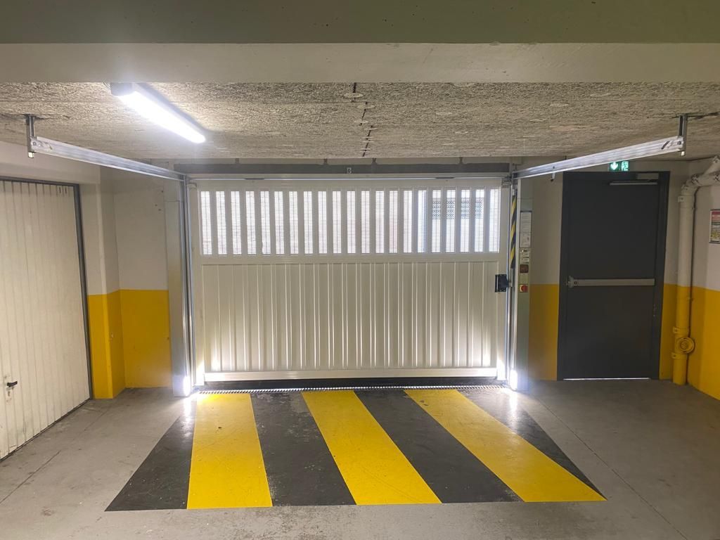 Rampe de parking souterrain avec bandes ralentisseurs jaunes et noires et portail fermé à l'extrémité