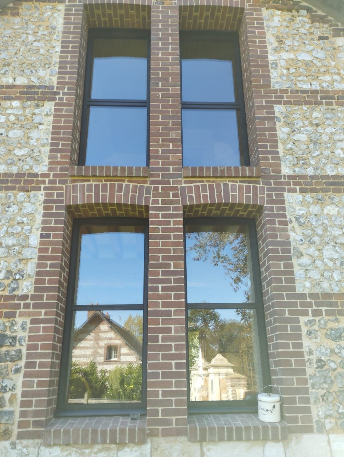 Fenêtres en briques avec encadrements sombres et reflets des maisons voisines