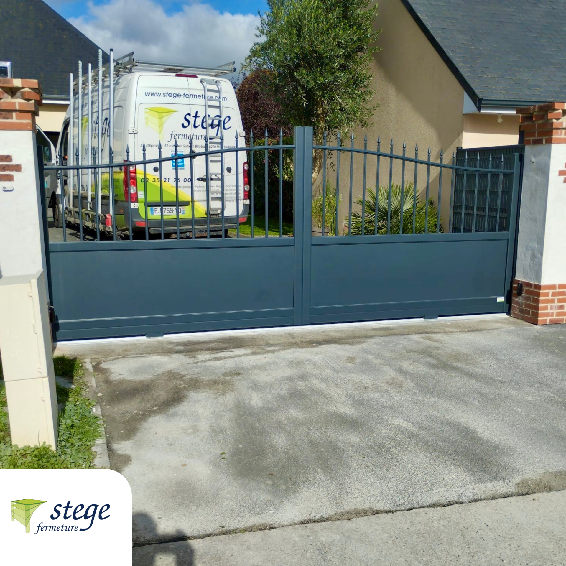 Allée avec un portail métallique bleu devant une camionnette et une maison, vue depuis la rue.