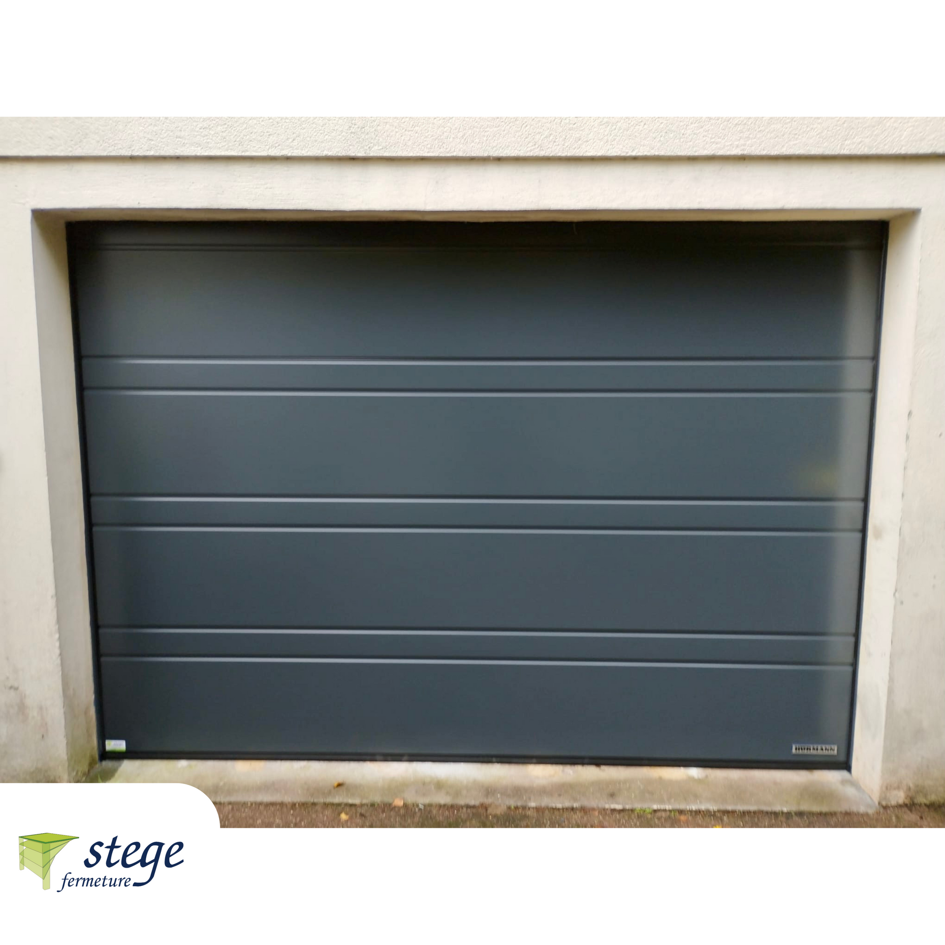 Porte de garage fermée gris foncé encastrée dans un mur beige.
