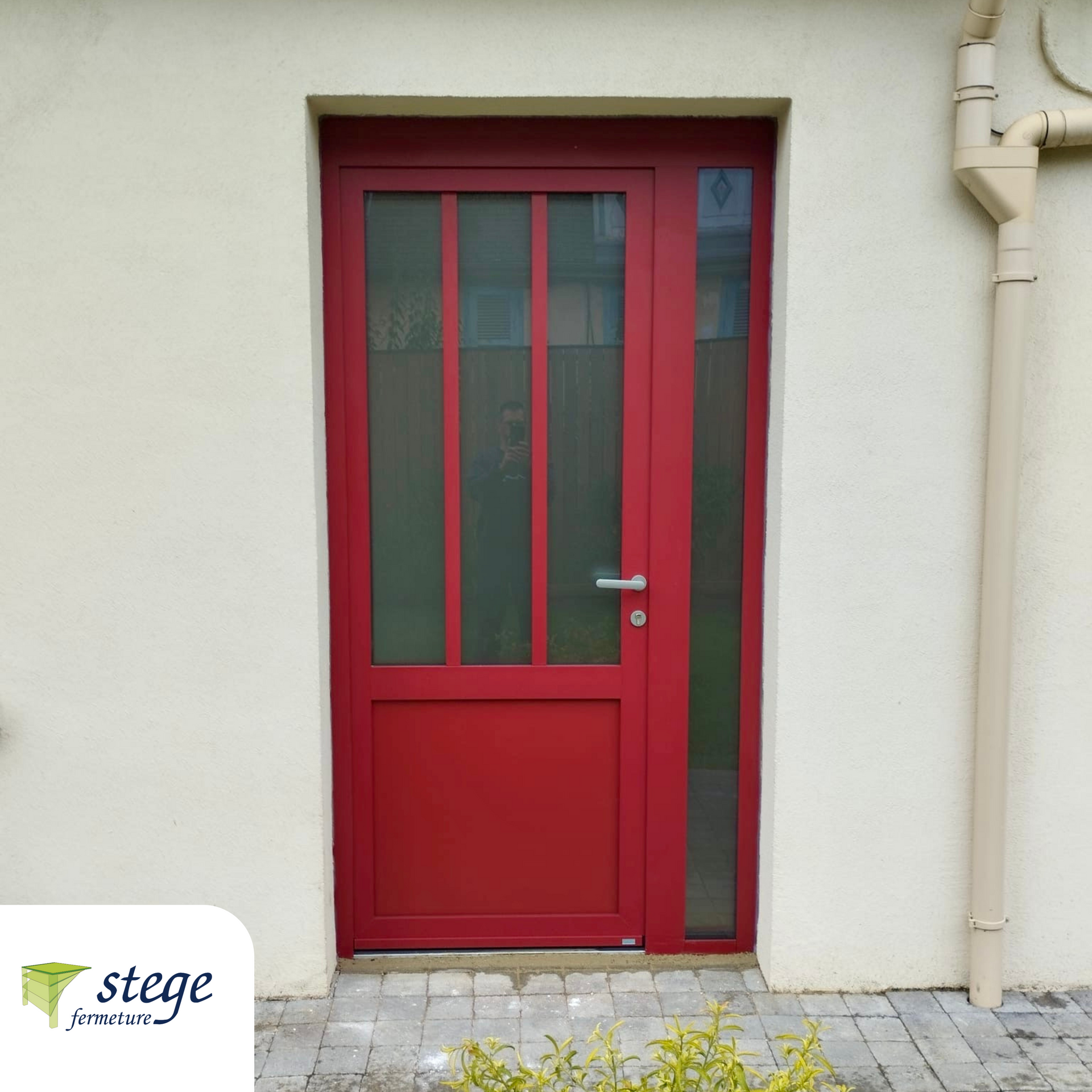 Porte d'entrée rouge avec panneaux de verre encastrée dans un mur extérieur beige