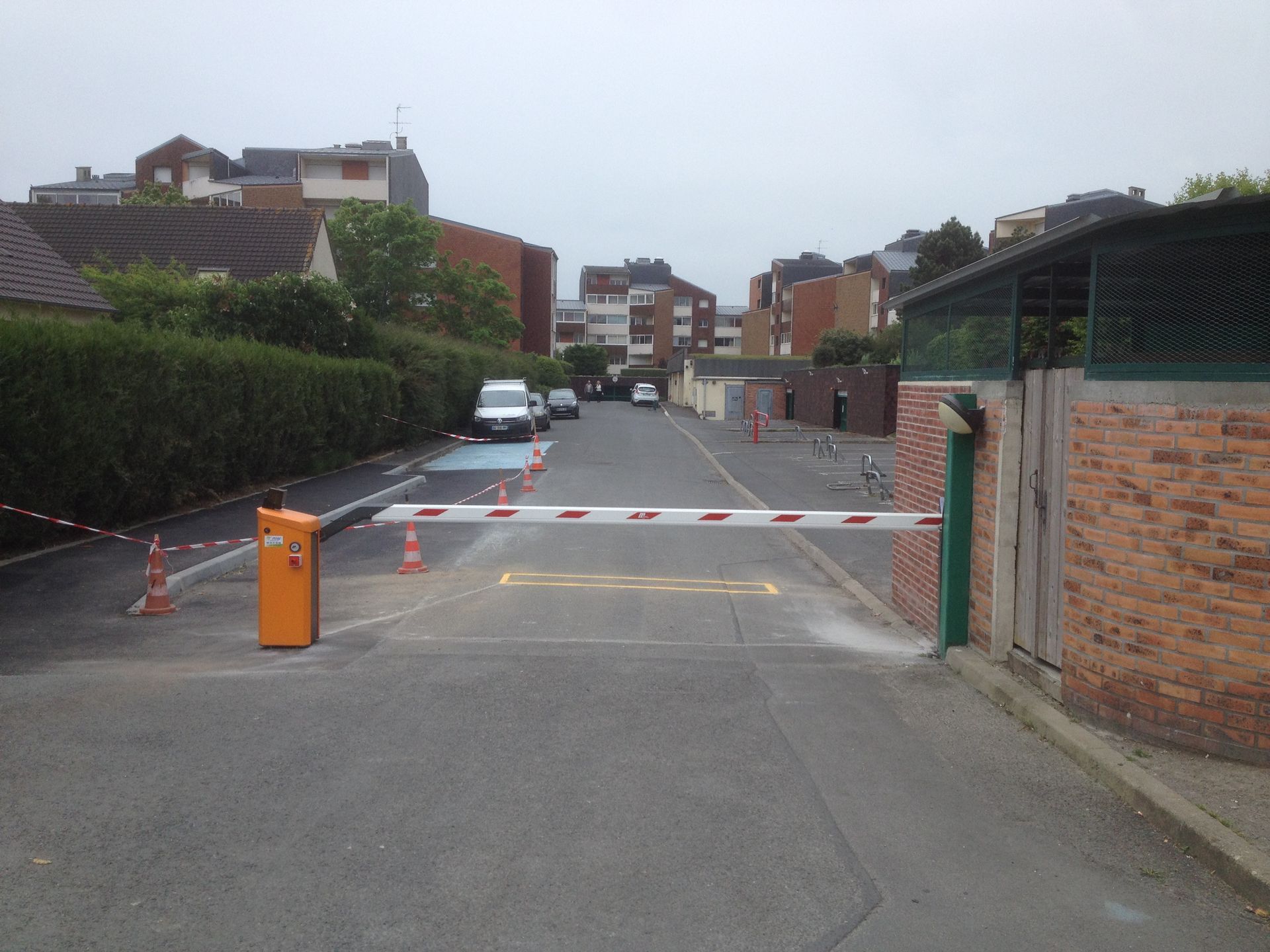Portail d'allée bloqué donnant sur une rue résidentielle avec des voitures garées et des maisons en briques au-delà.