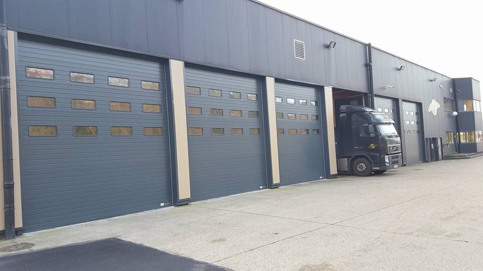 Entrepôt industriel avec portes de garage sectionnelles grises et un chariot élévateur noir stationné à l'extérieur.
