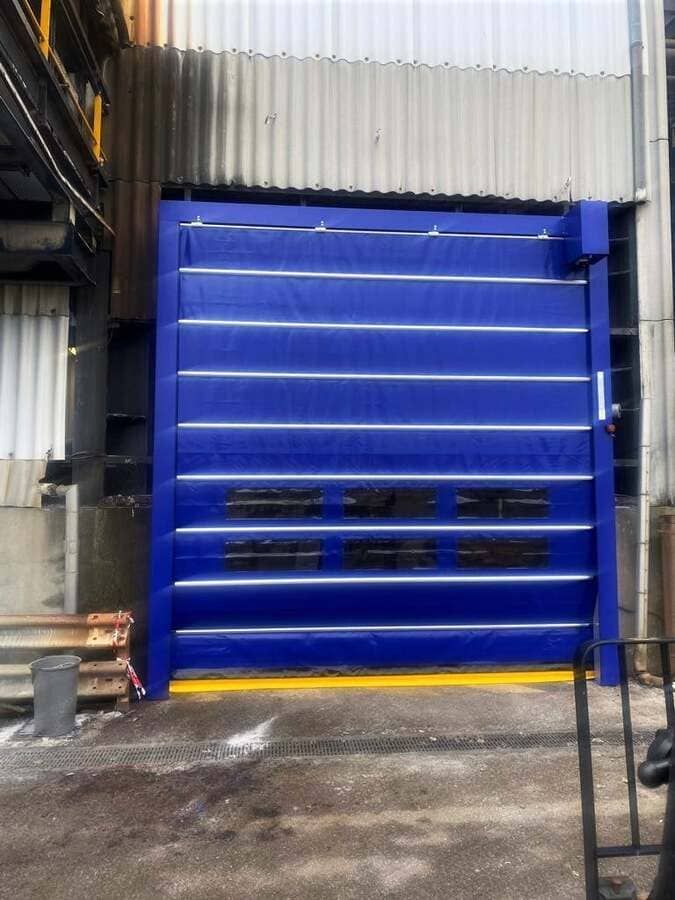Porte sectionnelle industrielle bleue dans un quai de chargement d'entrepôt aux parois métalliques ondulées.