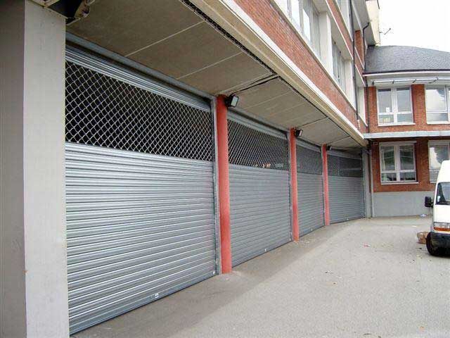 Rangée de volets métalliques gris fermés sous un passage couvert à côté d'un bâtiment
