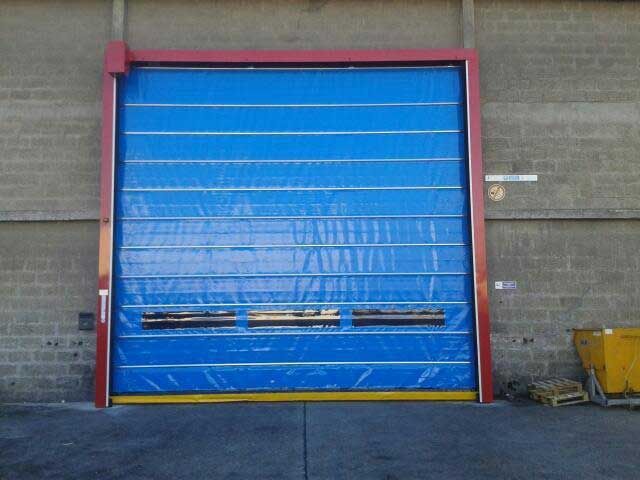 Porte sectionnelle industrielle bleue dans un mur de briques grises, avec de petites fenêtres horizontales près du bas.