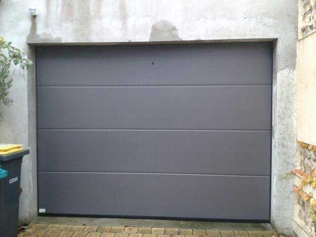 Porte de garage grise encastrée dans un mur en béton