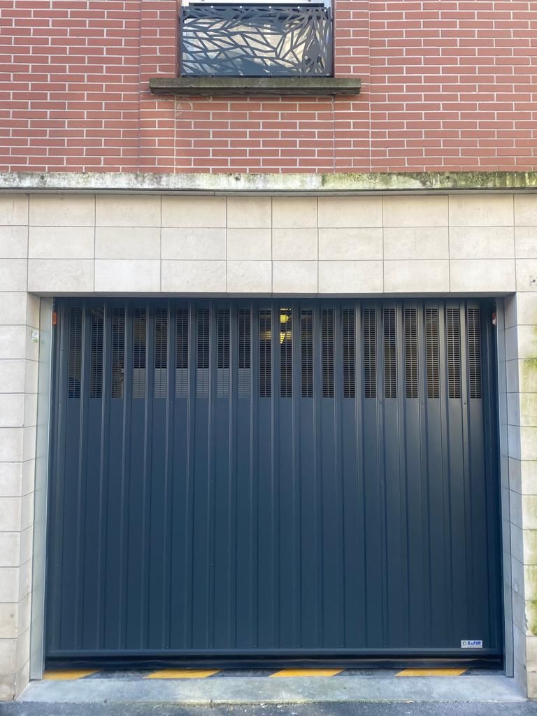 Porte de garage bleue encastrée dans une façade d'immeuble en briques à ossature de pierre