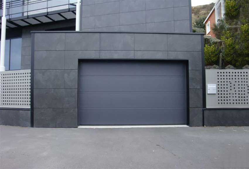 Porte de garage moderne gris foncé encastrée dans un mur en béton en bordure de rue