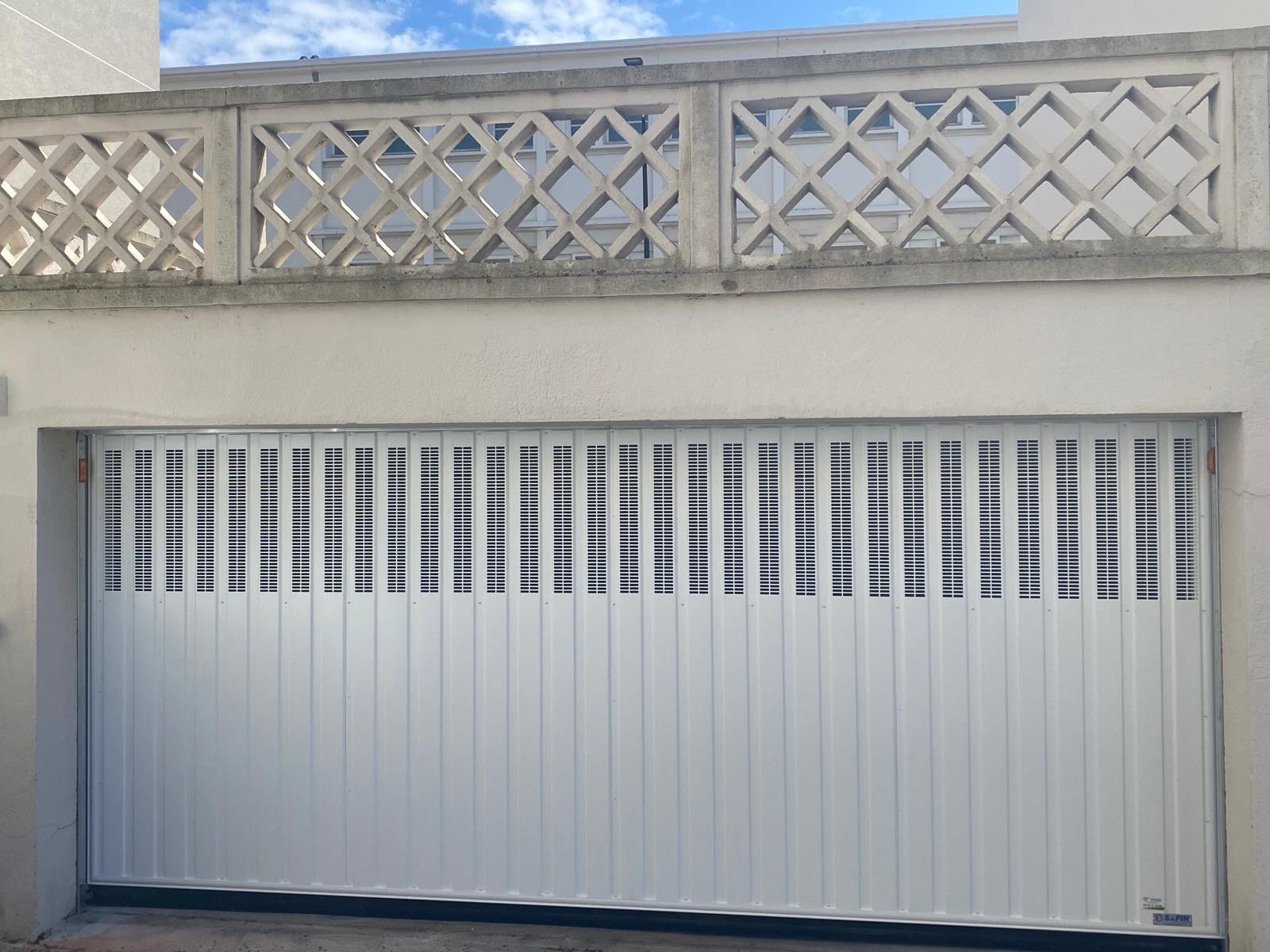 Porte de garage blanche avec fenêtres verticales étroites sous un mur décoratif en béton
