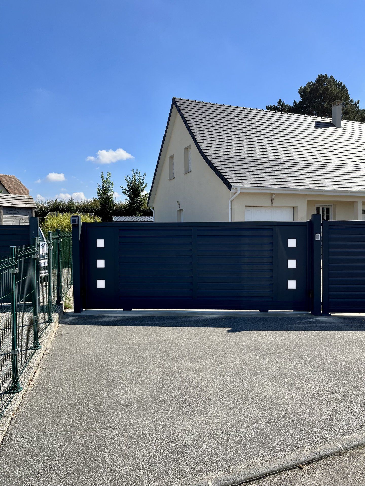 Portail coulissant noir devant une maison blanche sous un ciel bleu