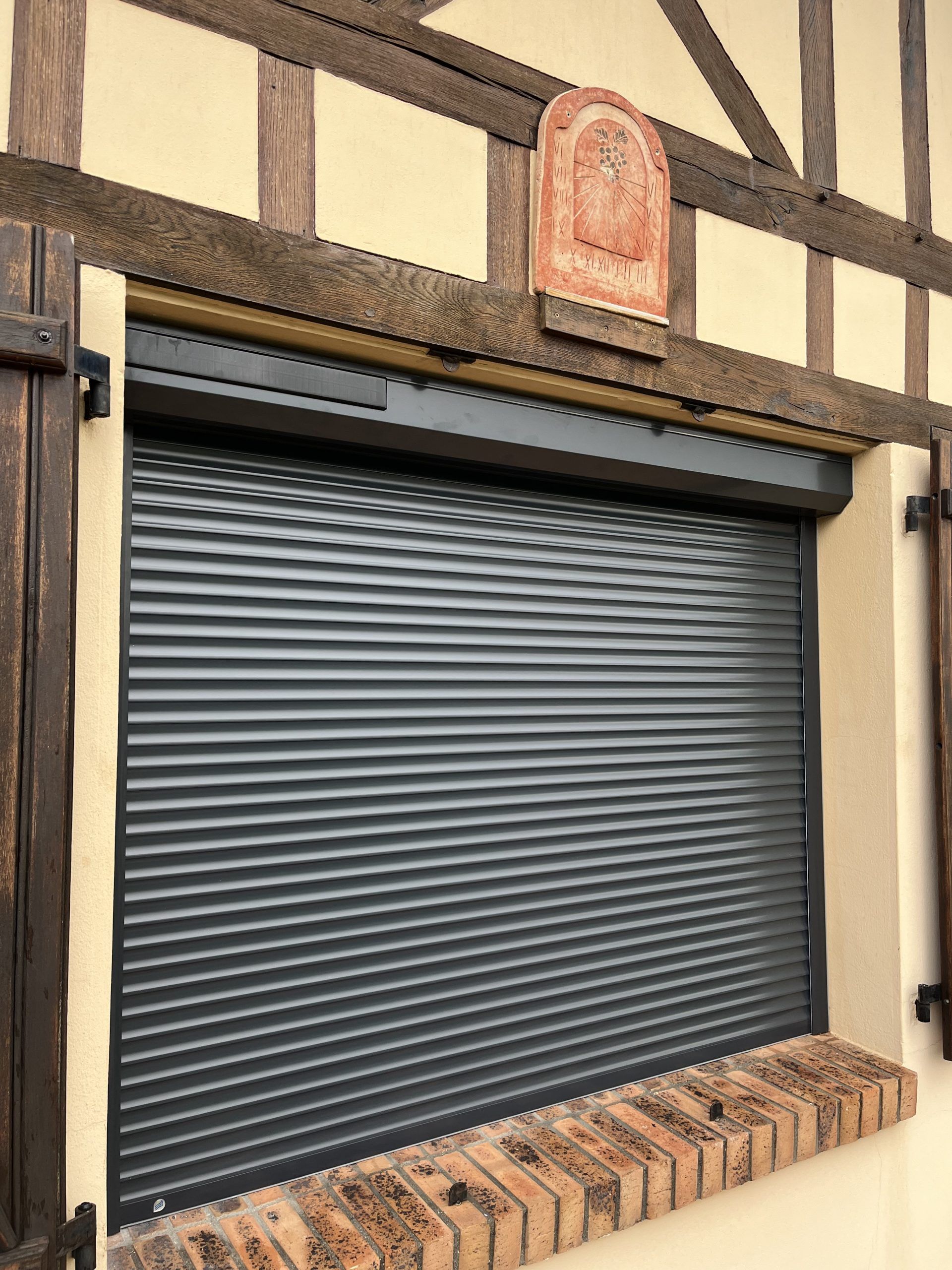Volet métallique gris foncé fermé sur une façade de bâtiment en briques et bois