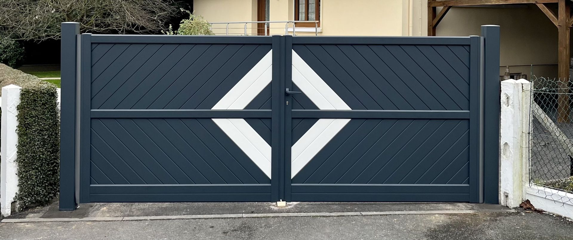 Portail coulissant moderne bleu foncé avec panneaux diagonaux blancs barrant une allée