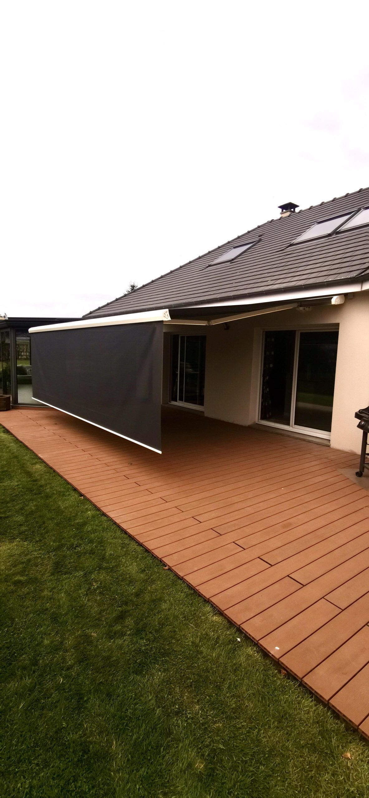 Terrasse pavée, pelouse et maison avec un auvent rayé sous un ciel couvert