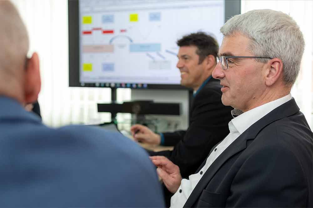 Ein Mann im Anzug und mit Brille sitzt vor einem Computerbildschirm.