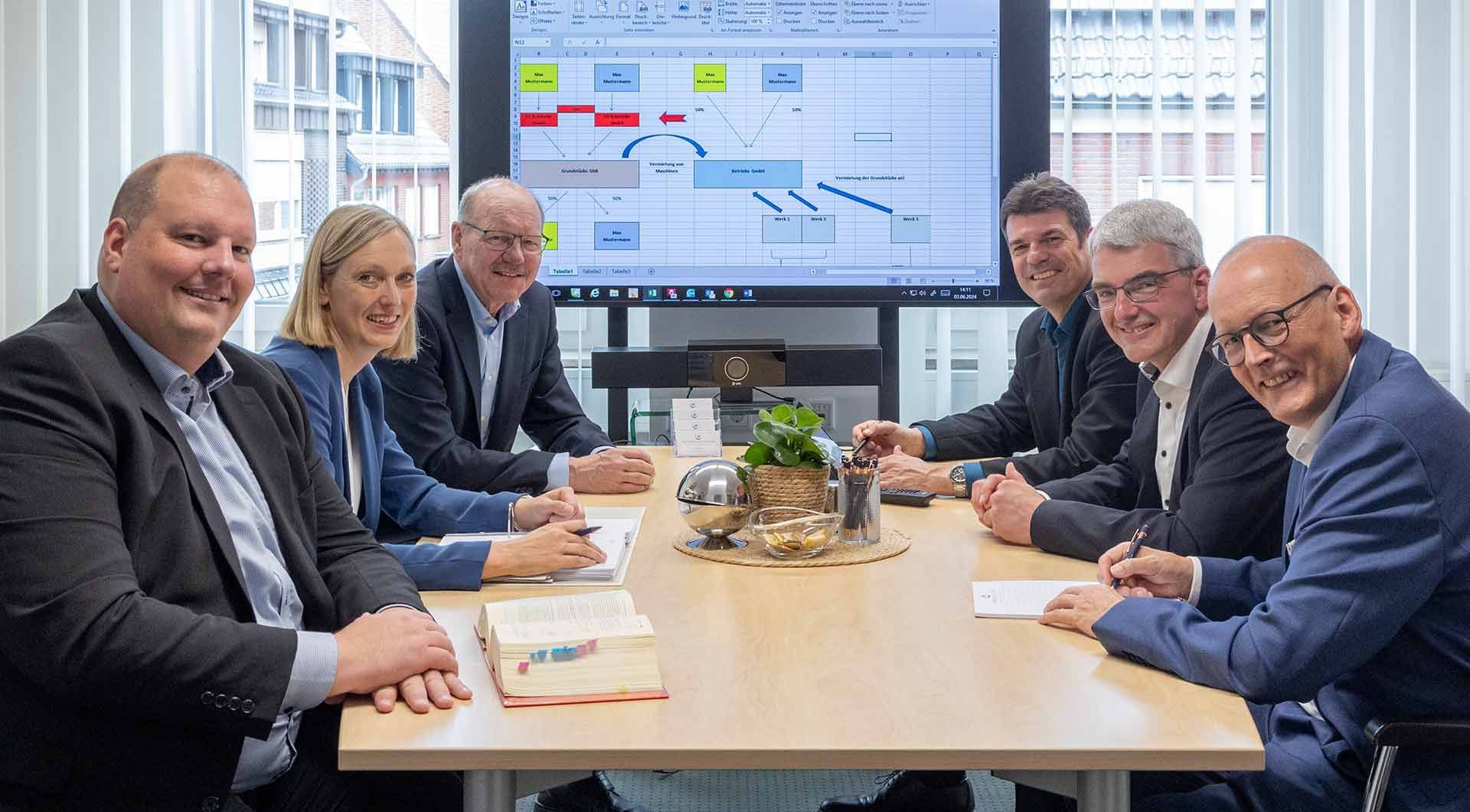 Eine Gruppe von Menschen sitzt um einen Konferenztisch vor einem großen Bildschirm.