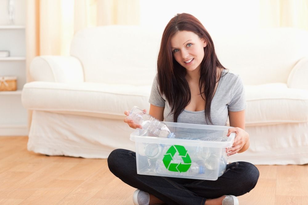 Una mujer está sentada en el suelo sosteniendo un contenedor de reciclaje.