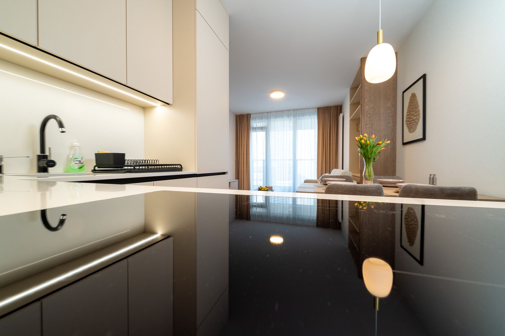 Modern kitchen with black glossy countertop, white cabinets, and a view to the window.