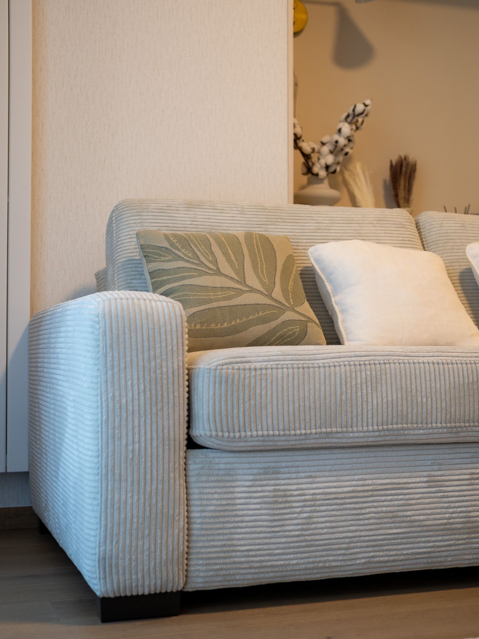 Light gray corduroy sofa with leaf and white pillows in a neutral-toned living room.