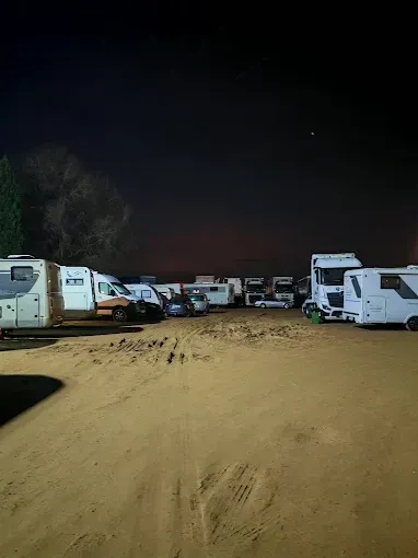Autocaravanas y camiones estacionados en un terreno de tierra por la noche; cielo oscuro arriba.