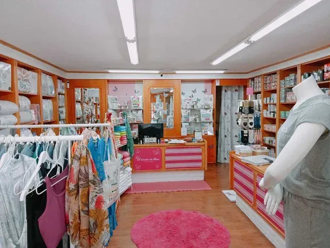 Interior luminoso de estilo boutique con alfombras rosas, percheros y estantes de exhibición bajo luces fluorescentes.